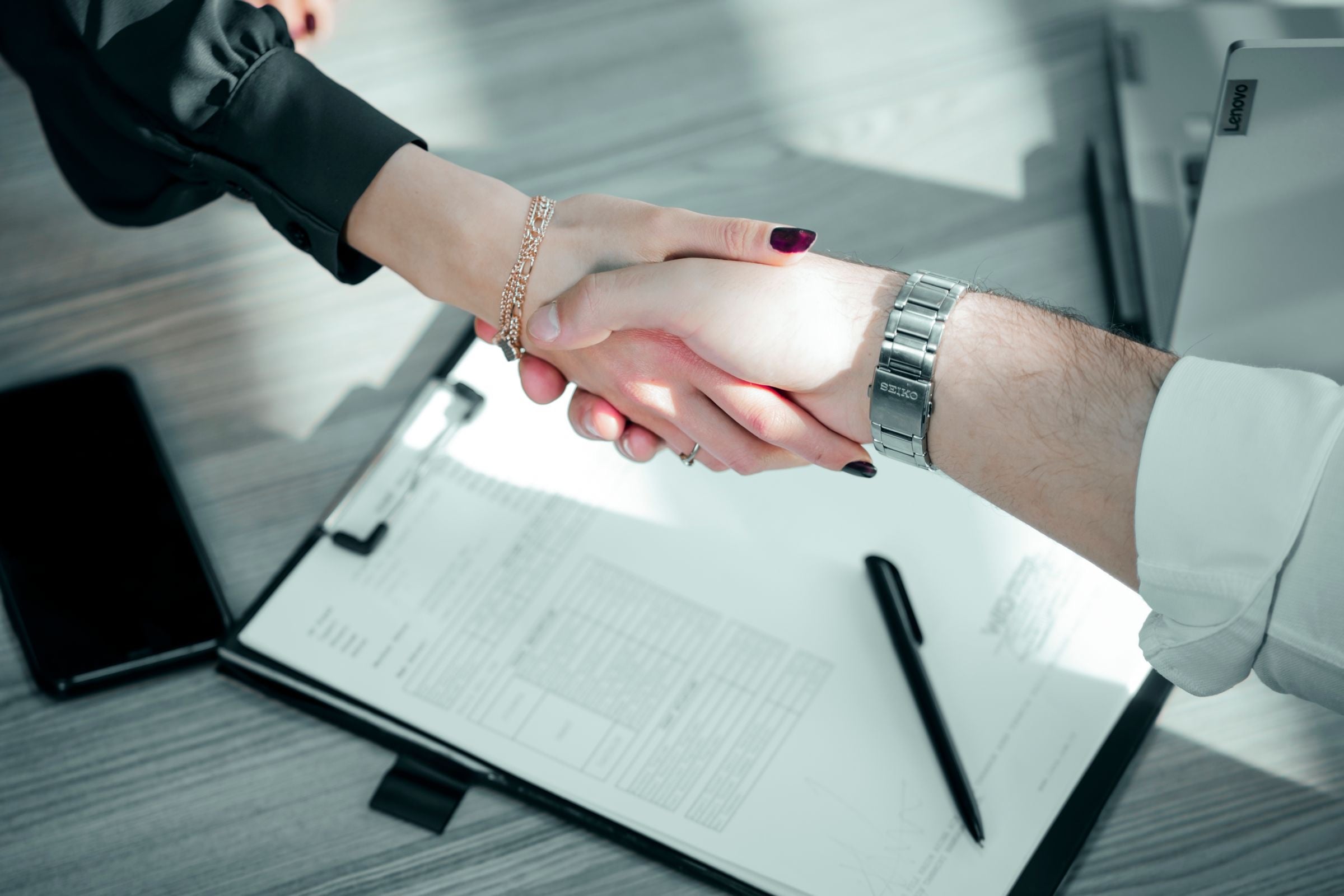 Two people shaking hands over a signed contract on a clipboard