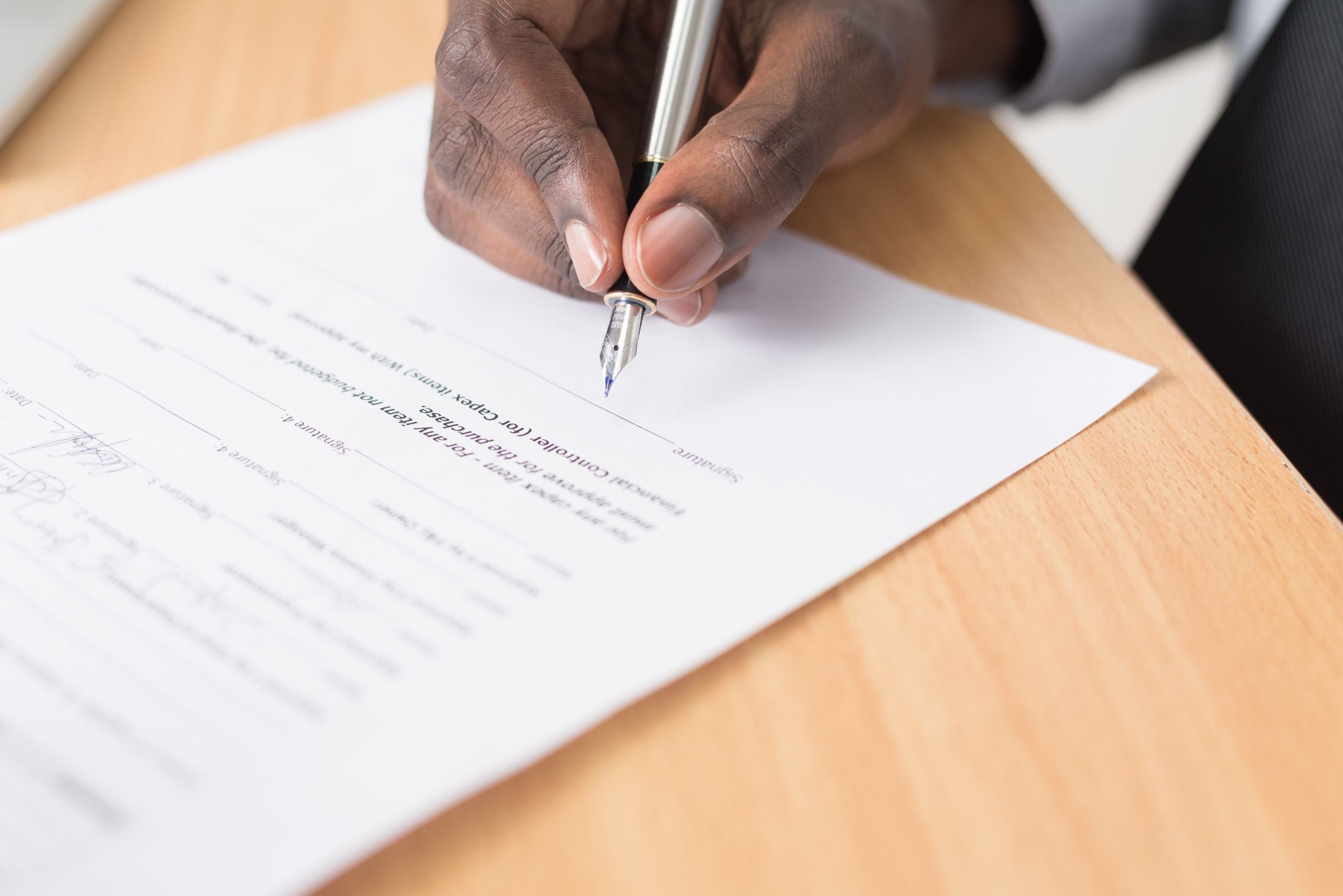A hand signing a printed document with a fountain pen