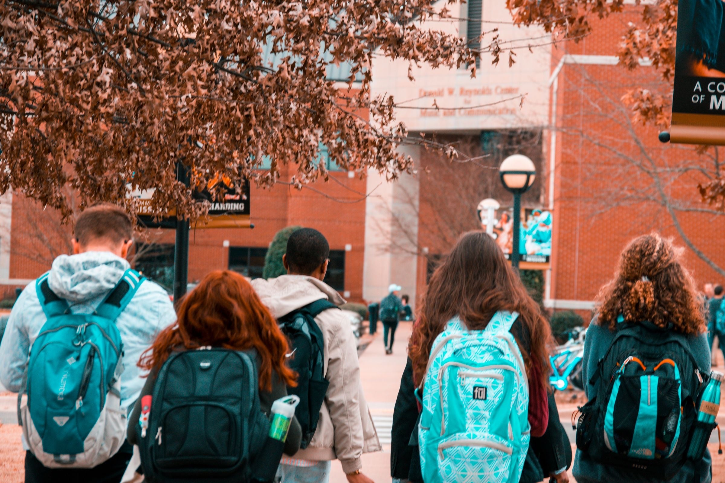 A group of university students with backpacks, seen from behind
