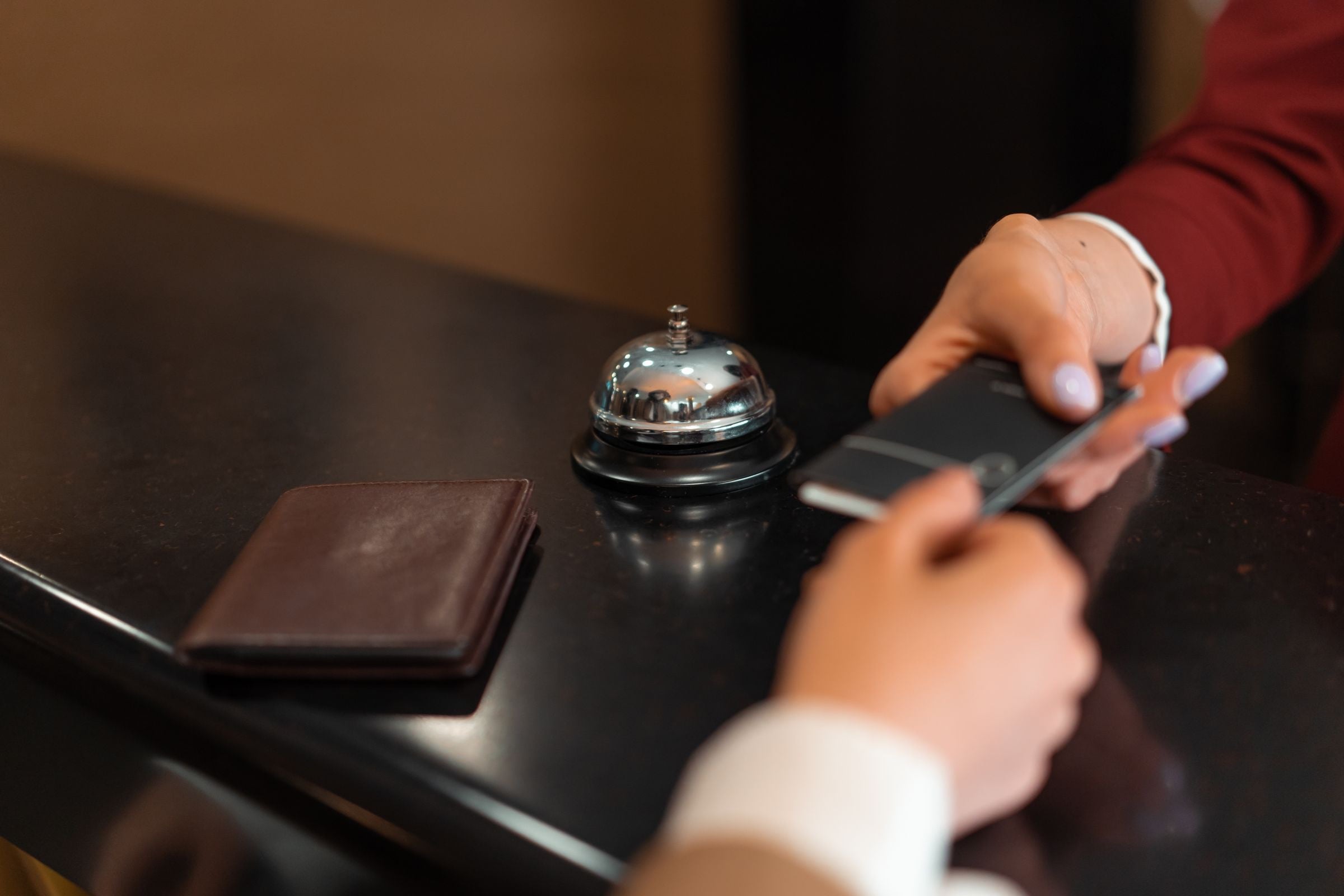 A guest handing over a card at a hotel reception desk beside a service bell
