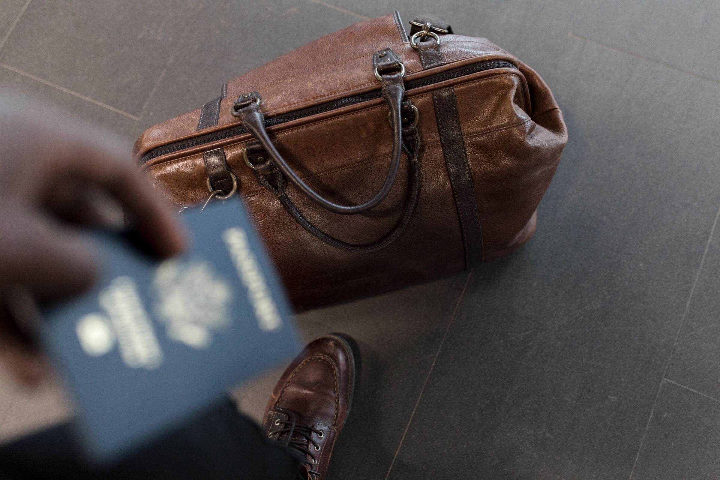 A passport held over a leather travel bag in an airport