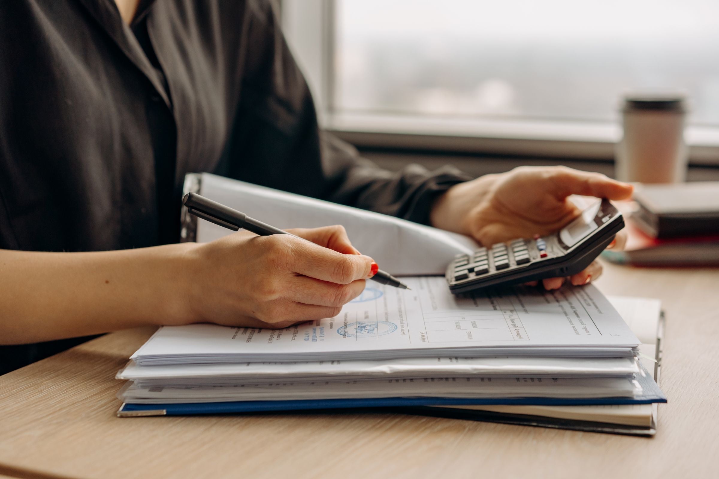 Hands using a calculator over a stack of payroll documents